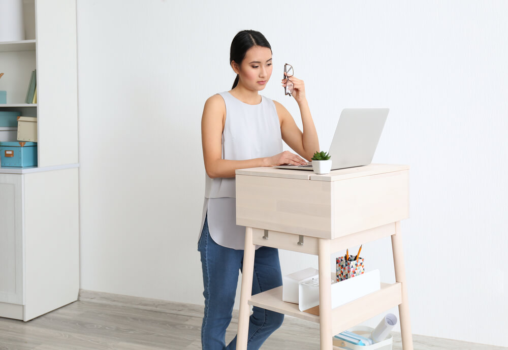 Asian woman typing on laptop at DIY stand-up desk