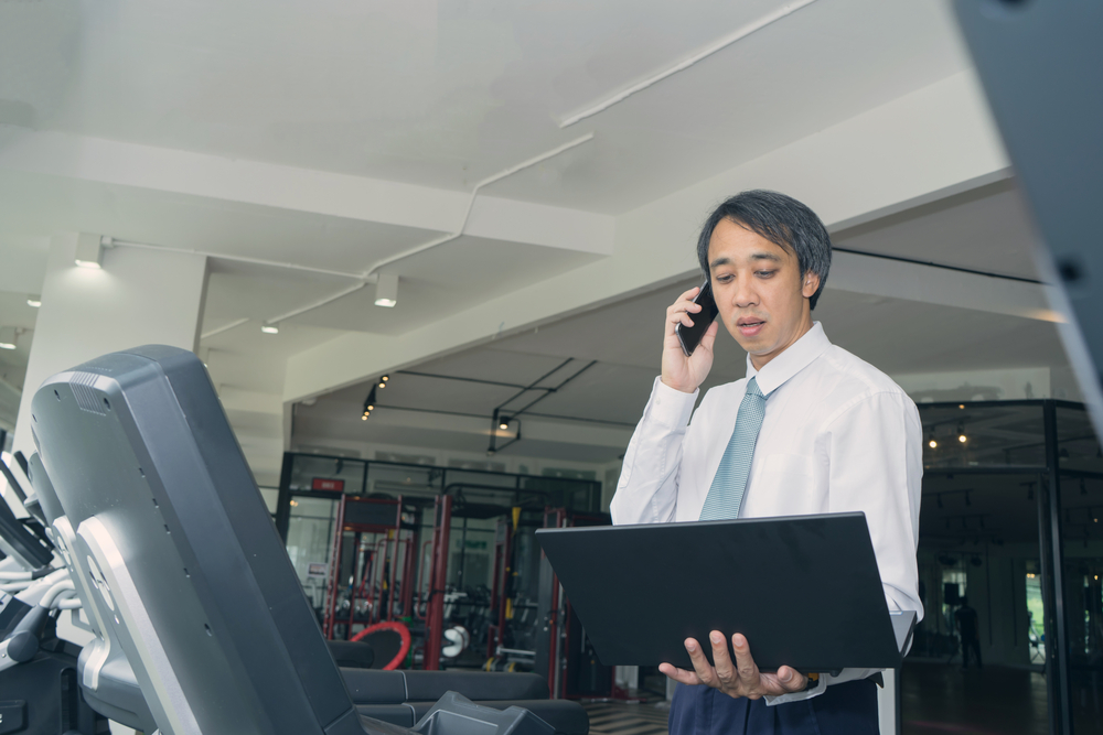 Businessman busy use smart phone and laptop on treadmill machine