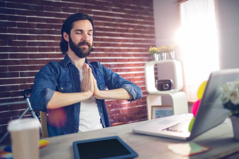 Businessman with hand clasped doing standing yoga poses in creative office