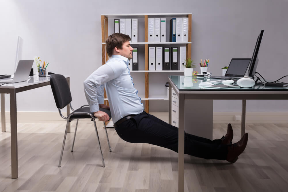 Young Businessman Doing Triceps Dips In Office