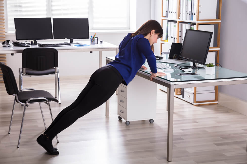 Young Businesswoman Doing Push Up On Office sit-stand Desk