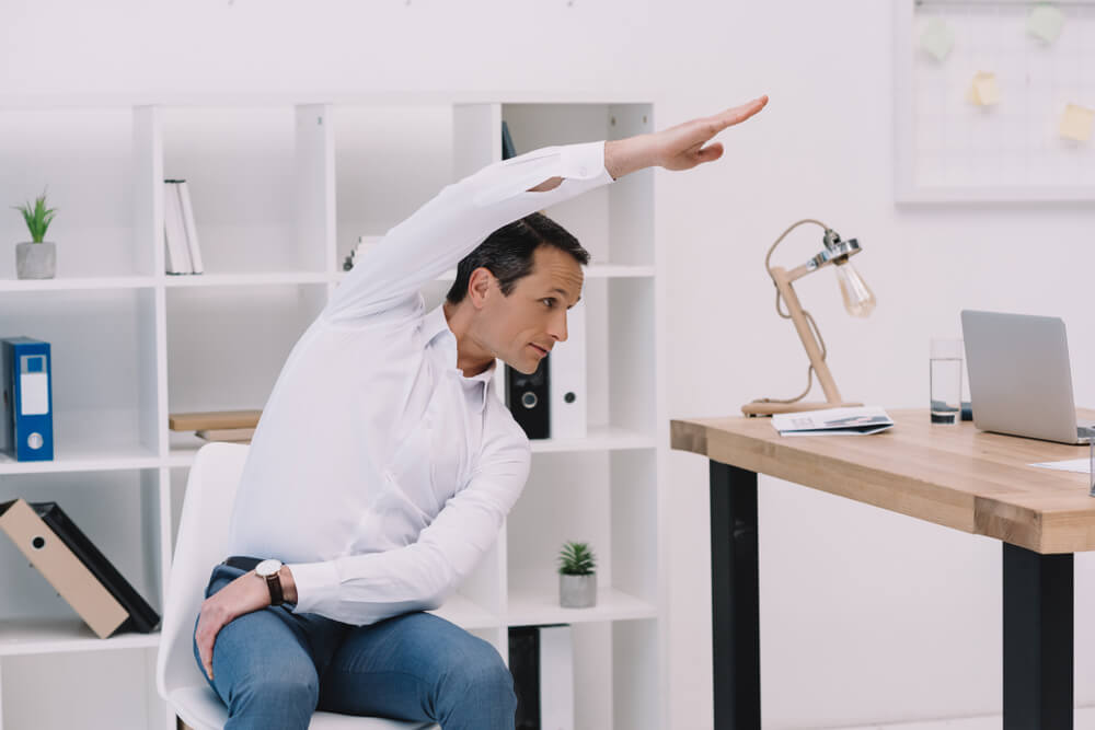 businessman doing side bend on his ergonomic chair 