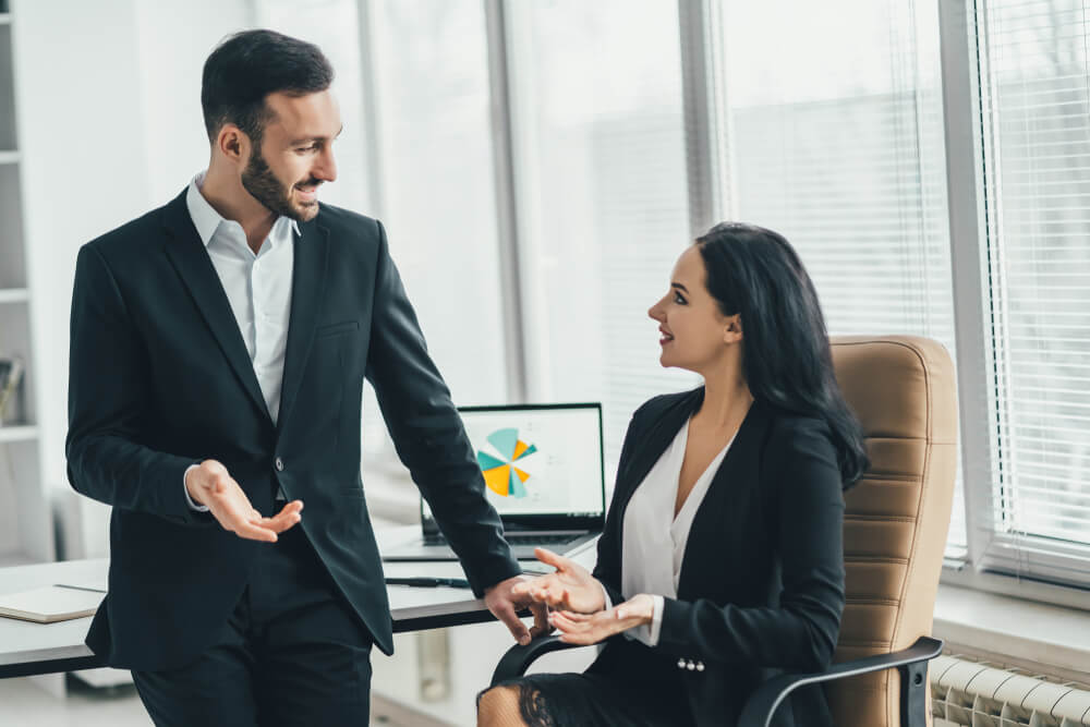  man and a woman are talking about sitting and standing at the office table