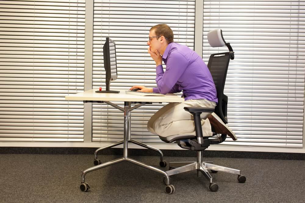 Office employee is sitting in slouching position on ergonomic chair