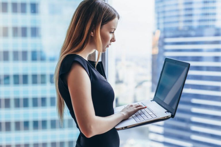 woman is holding laptop while standing at work