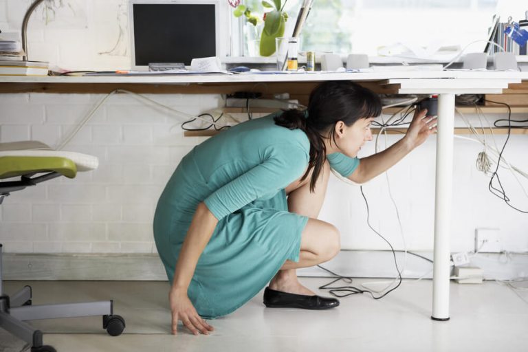 young businesswoman adjusting cables under desk